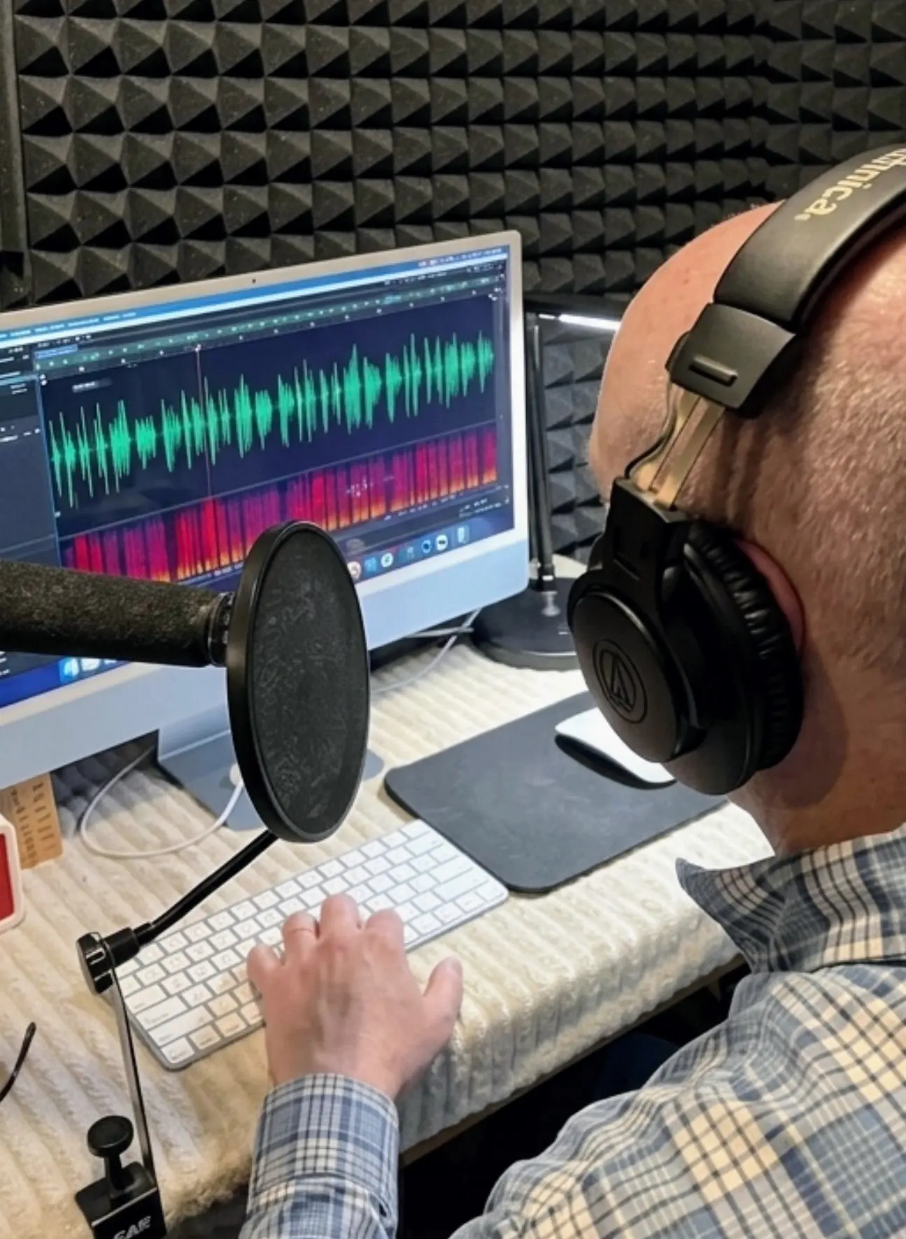Person recording audio in a soundproof room with headphones and microphone.
